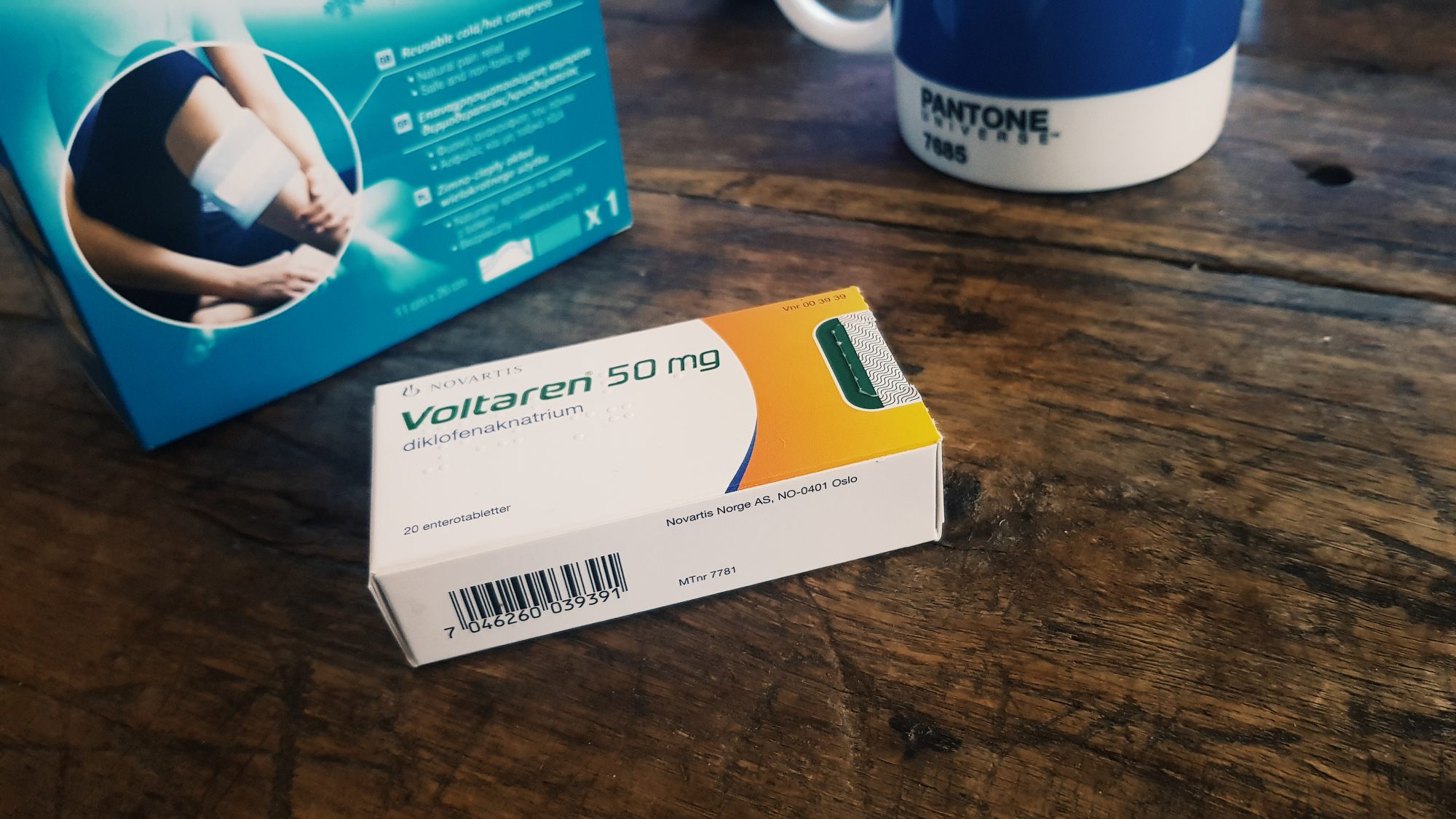 A packet of medicine on a table top, alongside a cup of tea. The medicine packet is in Norwegian language and reads 