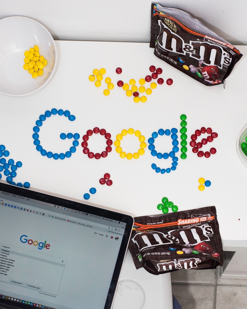 A photo of the Google logo made from coloured candy lay on a desk next to a laptop computer