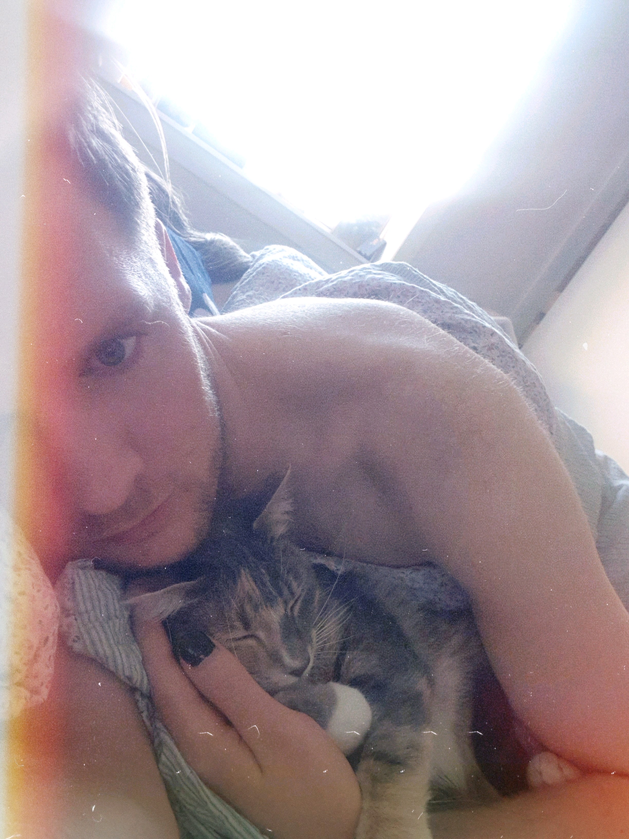 A photo of coxy lay in bed cuddling with a cute kitten, who is sleeping in his arms.