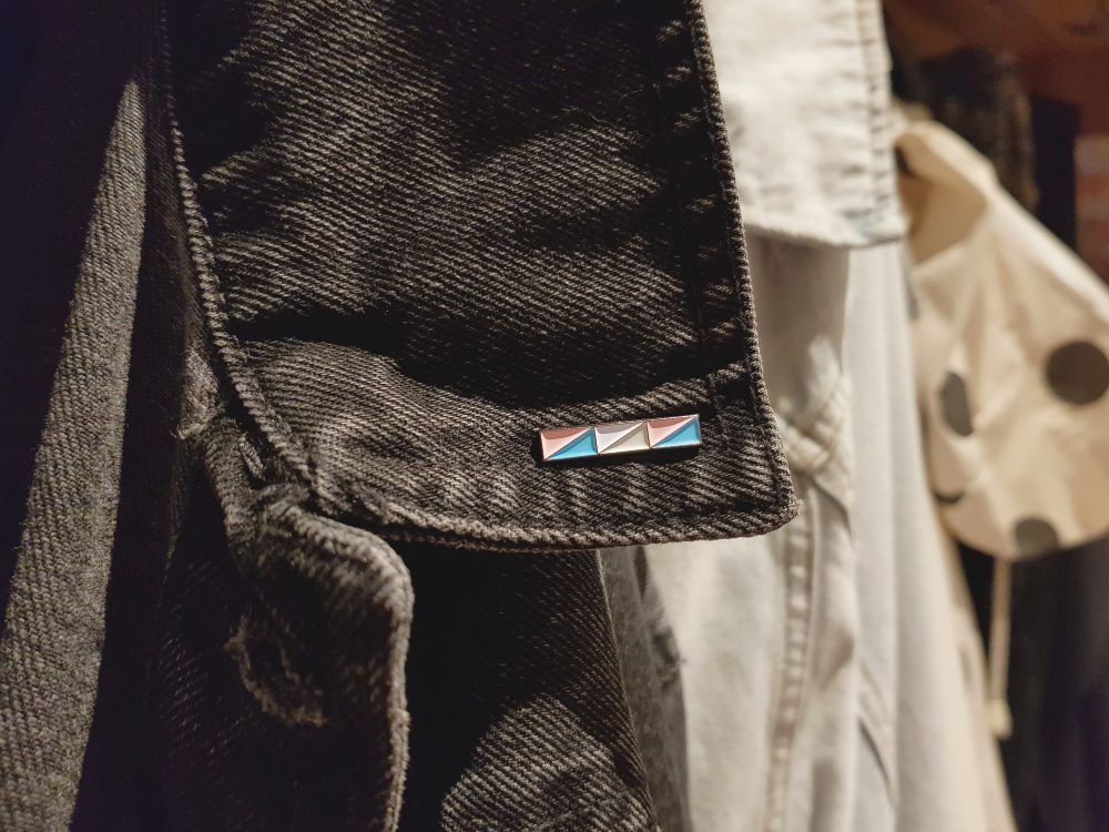 A photo of a transgender bar pin badge pinned to a black denim jacket