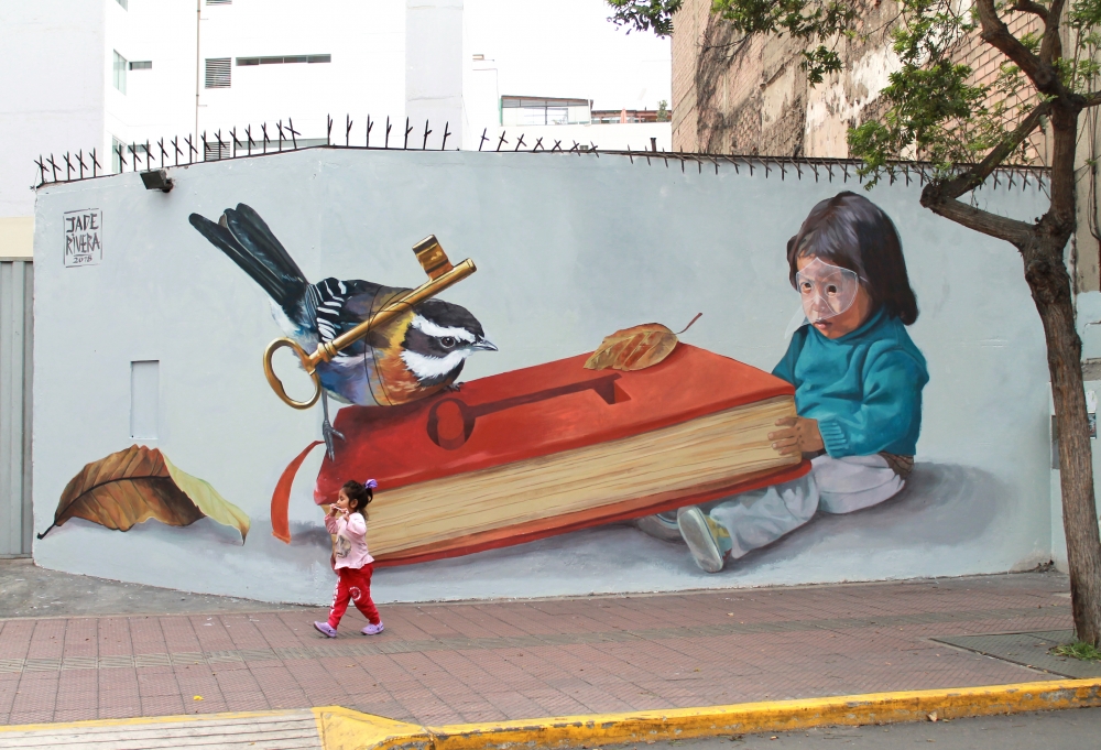 A young girl dressed in pink and red passes a wall featuring a mural of a bird pulling a key out from a book.