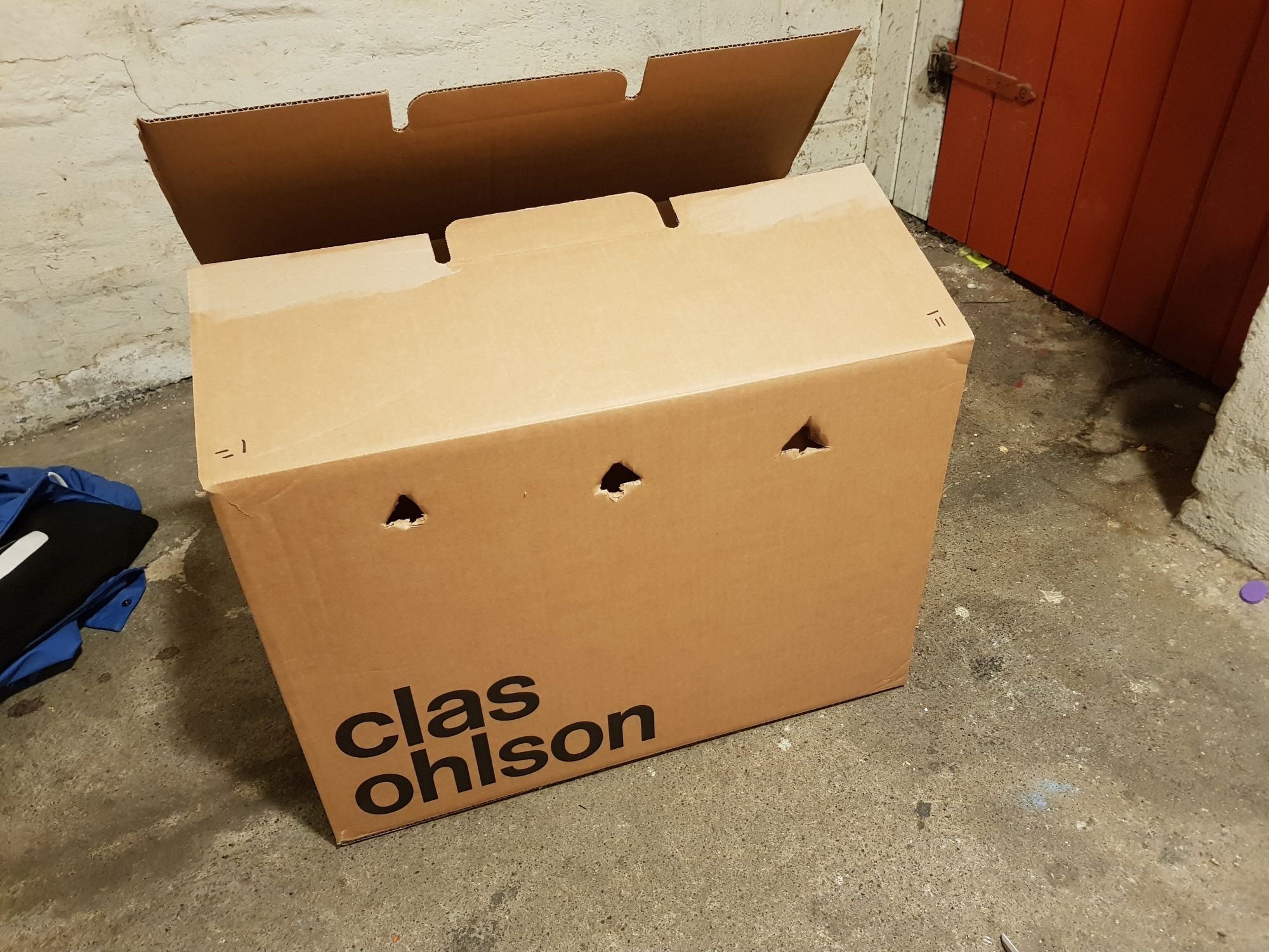 A photo of a cardboard box in a basement, open and with a few holes punched in the side to allow for breathing room. The box reads 