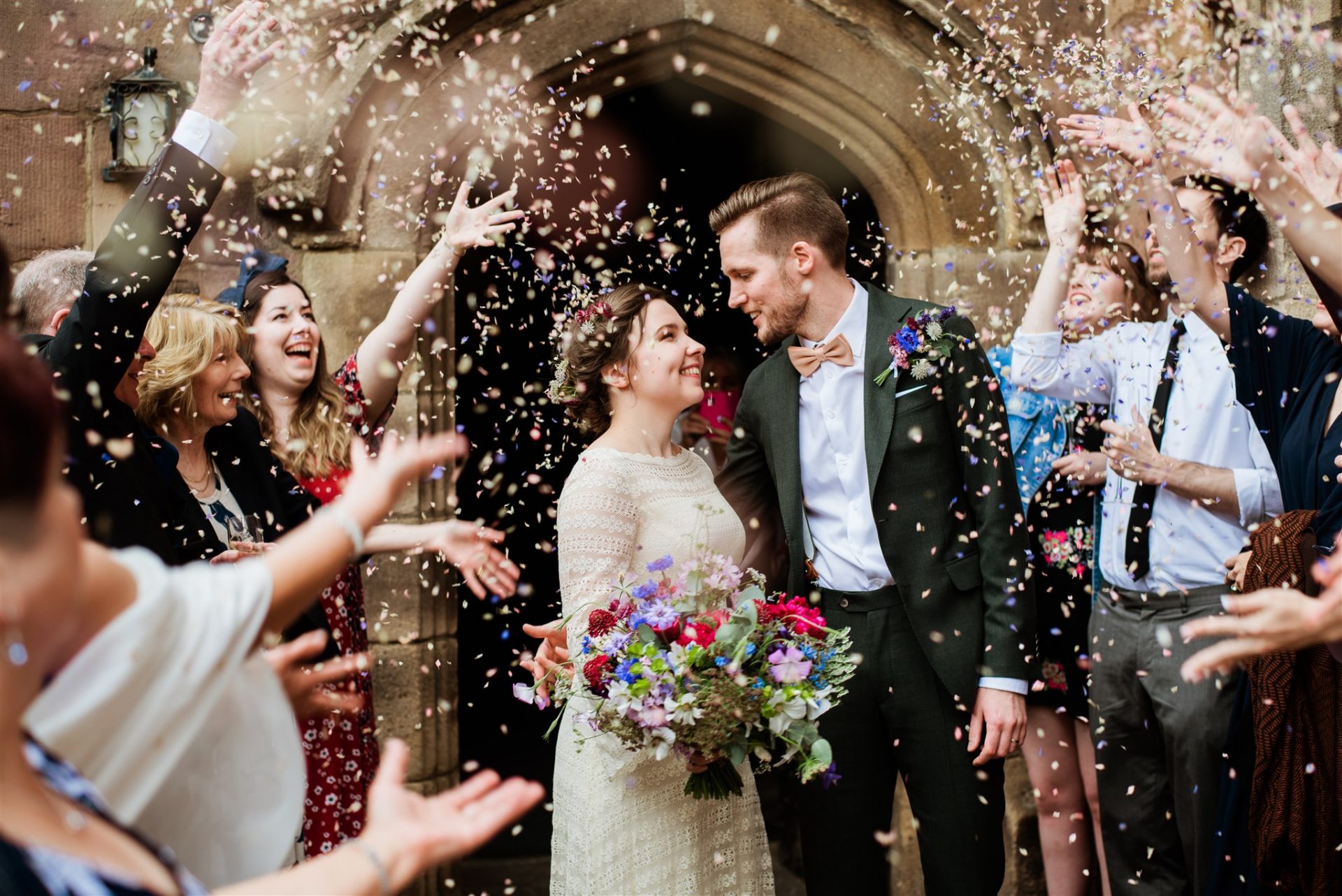 A photo of Matt and Ine leaving Chetham's Library down a tunnel of friends and confetti