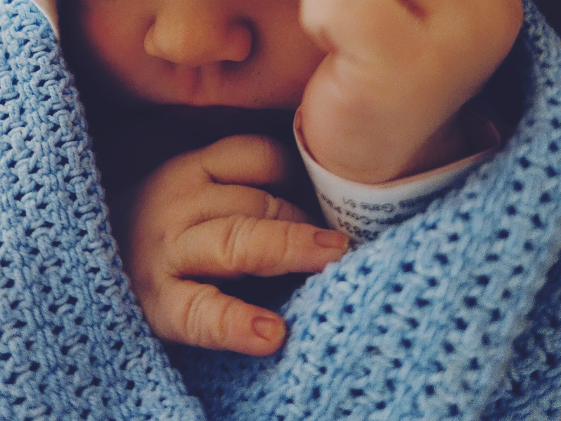 A close up photo of a baby, showing hands and nose and chin. The baby is wrapped in a blue blanket.