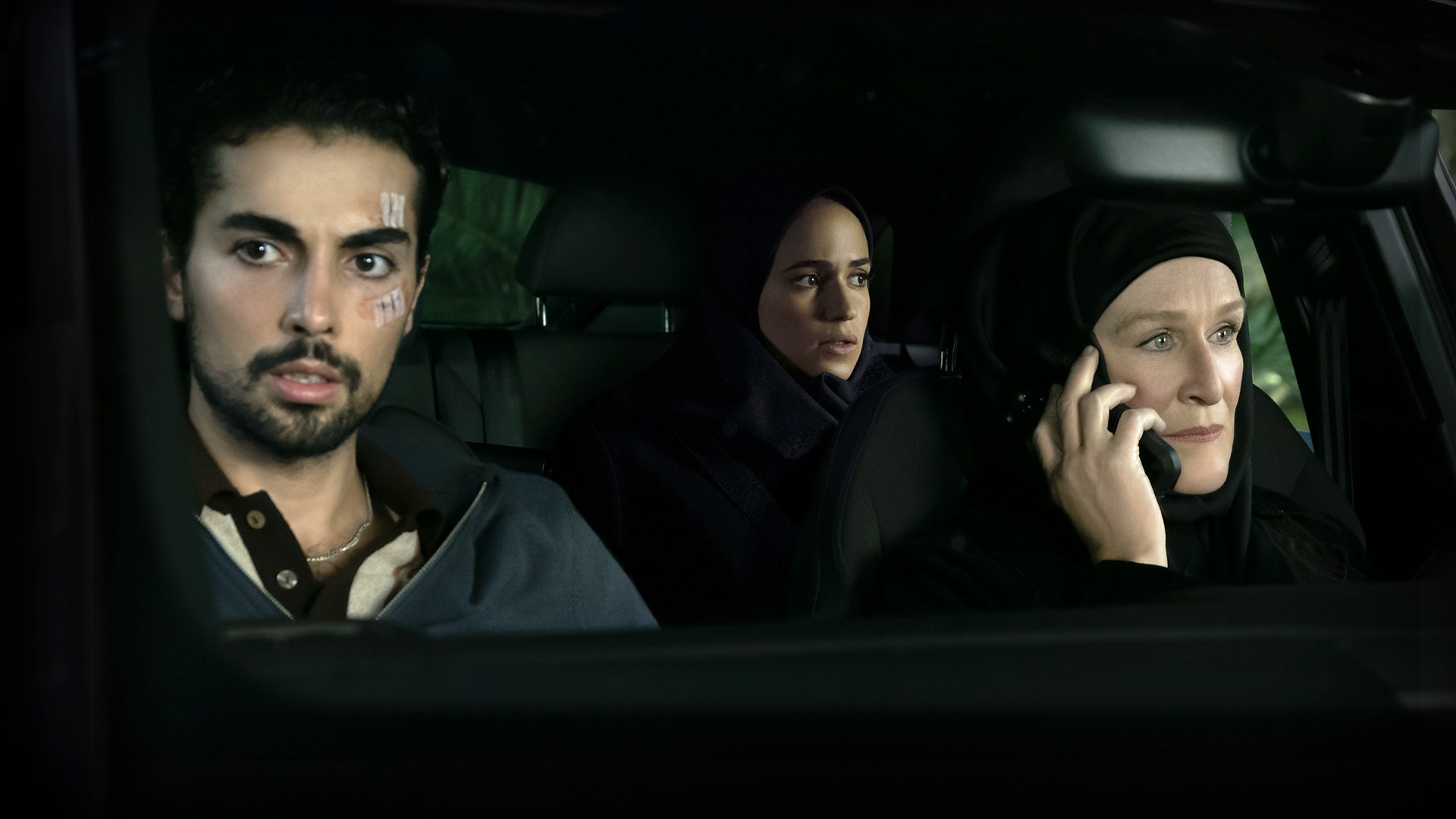 A screencap from the TV series Tehran with the lead character sat in the back seat of a car.